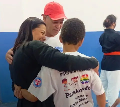 Mãe e pai abraçando o filho de camiseta do Parakobudo no tatame