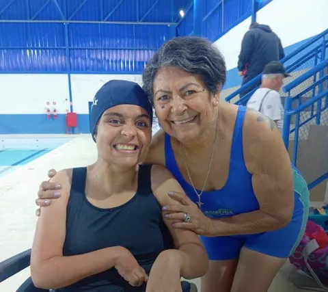 Duas pessoas sorrindo abraçadas à beira da piscina