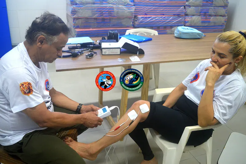 Atendimento de fisioterapia: professor colocando eletrodos no joelho de uma aluna sentada