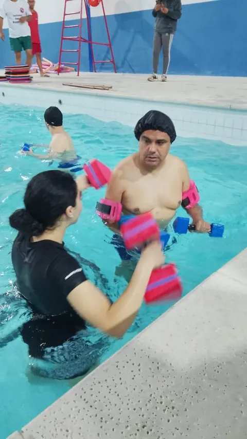 Exercício na água com halteres de espuma, acompanhado por uma professora