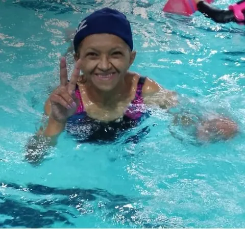Mulher sorrindo na água, fazendo sinal de paz